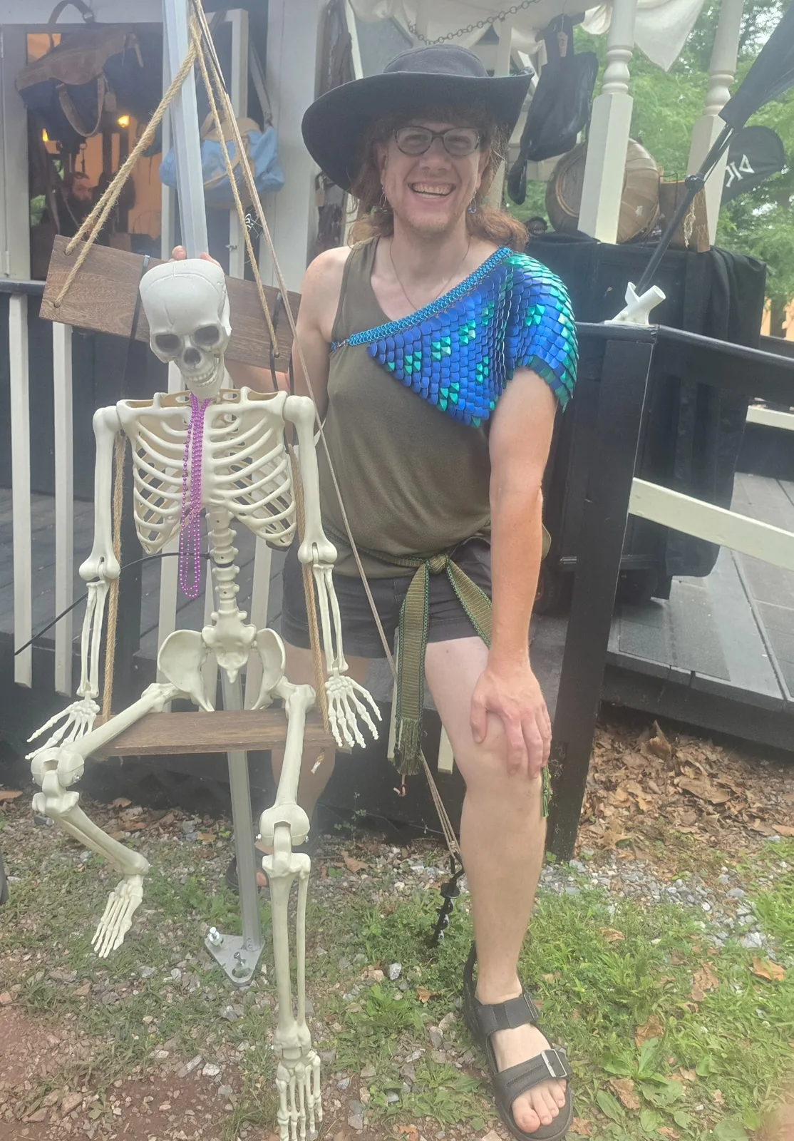 Model smiling beside a skeleton while wearing a blue and green scale shoulder drape