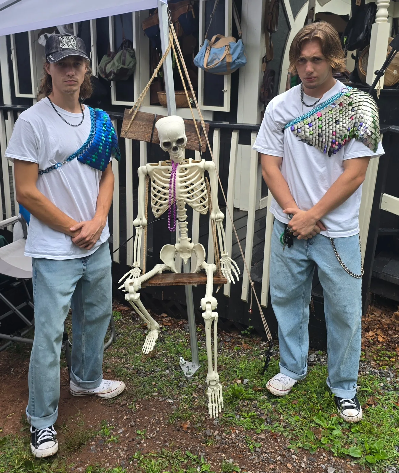 Two models posing with a skeleton while wearing blue and silver scale shoulder drapes